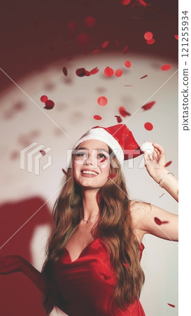Sexy happy woman with long hair in New Year's hat and red dress posing on white background at New Year's party style photo shoot 121255934