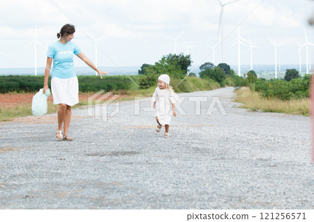 Happy and cheerful caucasian - white woman and little daughter are playing and walking together in nature with the beautiful windmills landscape in background. Mom is taking care of her daugher. Happy and cheerful caucasian - white woman and little daughter are playing and walking together in nature with the beautiful windmills landscape in background. Mom is taking care of her daugher. 121256571