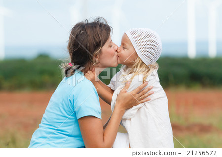 Happy and cheerful caucasian - white woman and little daughter are playing and walking together in nature with the beautiful windmills landscape in background. Mom is taking care of her daugher. 121256572