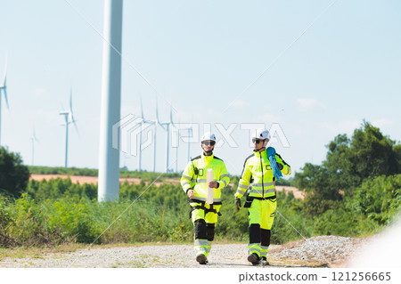 Team of professional electrical engineers in fully safety suit are working and discussing together at the windmill electric generating turbine. Electricians working at the site of windmill turbine. Team of professional electrical engineers in fully safety suit are working and discussing together at the windmill electric generating turbine. Electricians working at the site of windmill turbine. 121256665