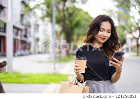 Smart and good looking Asian businesswoman is walking in the city while using a smartphone for text message and talking to colleague and other hand holding a coffee cup. Business woman portrait. Smart and good looking Asian businesswoman is walking in the city while using a smartphone for text message and talking to colleague and other hand holding a coffee cup. Business woman portrait. 121256851