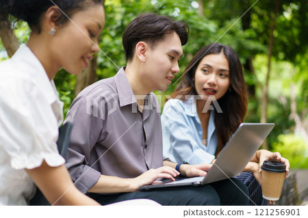 Diverse ethnicity university students are discussing together on laptop or notebook computer outside at park, people talking about the business on laptop computer outdoor. Modern working lifestyles. 121256901