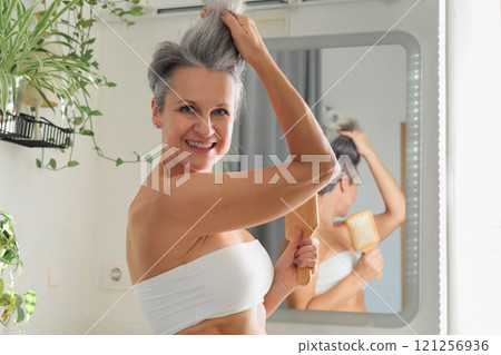 Portrait funny mature gray haired woman at light bathroom with hairbrush closeup Portrait funny mature gray haired woman at light bathroom with hairbrush closeup 121256936