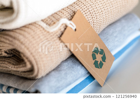 Knitted warm clothes neatly folded heap with craft tag recycling material circle arrow closeup 121256940