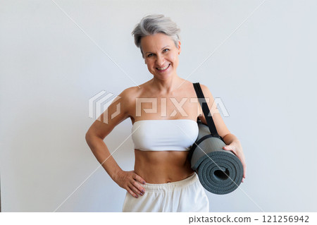Smiling mature gray haired sport woman with yoga roll mat posing isolated on white background Smiling mature gray haired sport woman with yoga roll mat posing isolated on white background 121256942