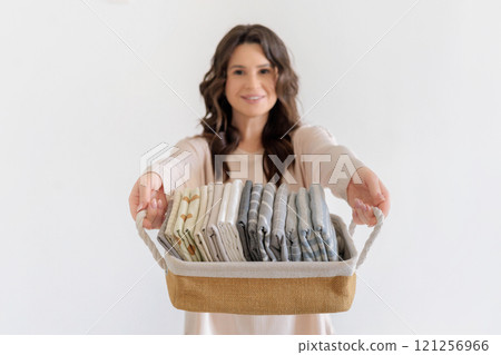 Beautiful European woman in beige suit holds wicker stylish basket with neatly folded pillowcases 121256966
