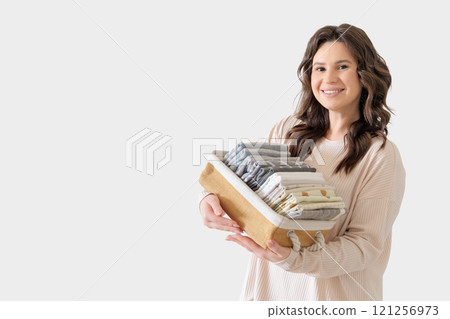 Beautiful European woman in beige suit holds wicker stylish basket with neatly folded pillowcases Beautiful European woman in beige suit holds wicker stylish basket with neatly folded pillowcases 121256973