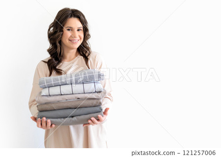 Young European beautiful woman holds neat stack of stylish bed linen in natural colors. Young European beautiful woman holds neat stack of stylish bed linen in natural colors. 121257006