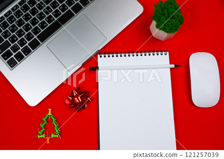 In the center of the photo is a white notebook with a black spring and a pencil, around it are a gray laptop with a black keyboard, a creative Christmas tree consisting of green pushpins, a white In the center of the photo is a white notebook with a black spring and a pencil, around it are a gray laptop with a black keyboard, a creative Christmas tree consisting of green pushpins, a white 121257039