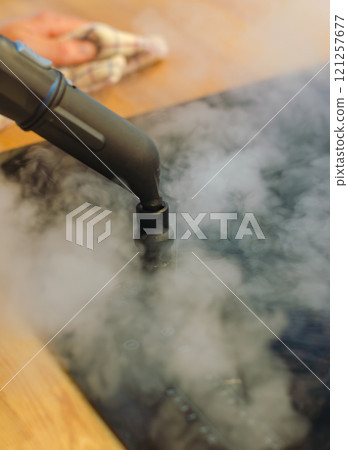 Close-up of a steam cleaner nozzle releasing steam onto induction stove . High quality photo 121257677