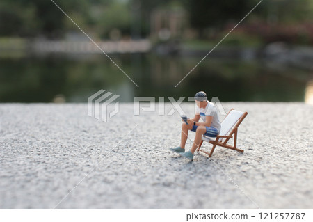 Miniature Person Relaxing on Deck Chair by Tranquil Lake Miniature Person Relaxing on Deck Chair by Tranquil Lake 121257787