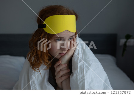 A woman in a bright yellow sleep mask sits comfortably on a bed 121257972