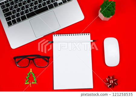 In the center of the photo is a white notebook with a black spring and a pencil, around it are a gray laptop with a black keyboard, a creative Christmas tree consisting of green pushpins, a white 121258535