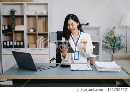 Confident business expert attractive smiling young woman typing laptop and holding digital tablet on desk in office. 121259737