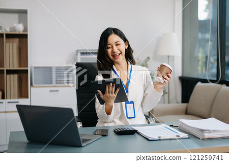 Confident business expert attractive smiling young woman typing laptop and holding digital tablet on desk in office. 121259741