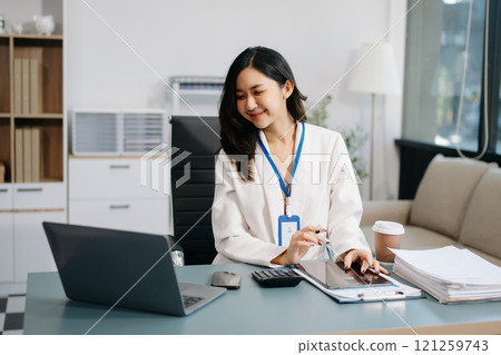 Confident business expert attractive smiling young woman typing laptop and holding digital tablet on desk in office. 121259743