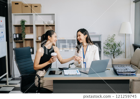Businesswomen work and discuss their business plans. A woman employee explains and shows her colleague the results paper Businesswomen work and discuss their business plans. A woman employee explains and shows her colleague the results paper 121259745