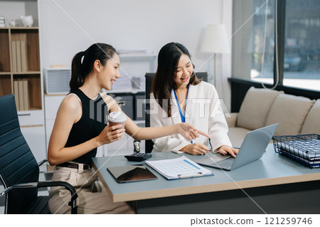 Businesswomen work and discuss their business plans. A woman employee explains and shows her colleague the results paper Businesswomen work and discuss their business plans. A woman employee explains and shows her colleague the results paper 121259746