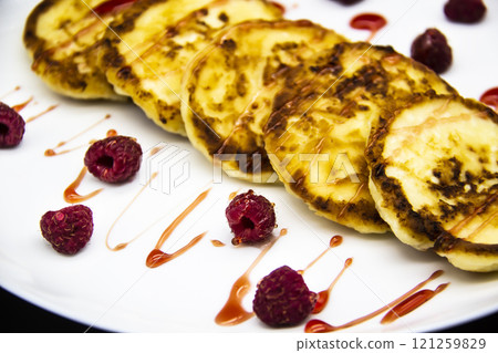 Ukrainian cottage cheese fritters, syrniki with jam on white plate. Cheese pancakes with raspberry without GMO. Delicious breakfast food at the morning. 121259829