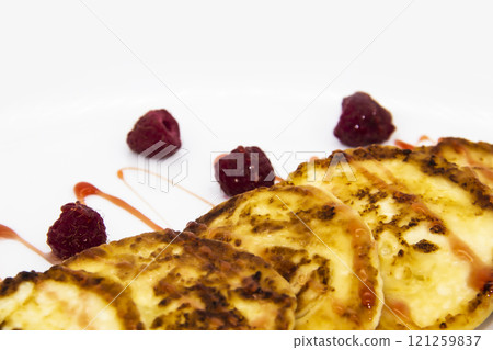 Ukrainian cottage cheese fritters, syrniki with jam on white plate. Cheese pancakes with raspberry without GMO. Delicious breakfast food at the morning. 121259837