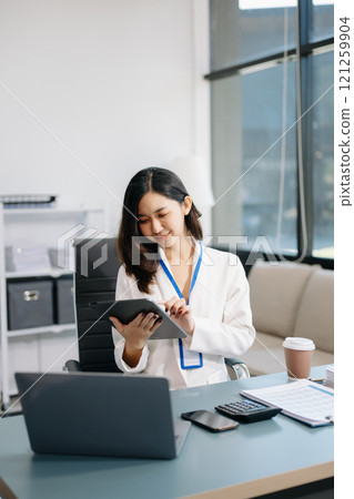 Confident business expert attractive smiling young woman typing laptop and holding digital tablet on desk in office. 121259904