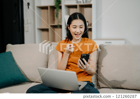 Young asian woman relax on comfortable couch at home texting messaging on smartphone and tablet smiling girl use cellphone 121260287