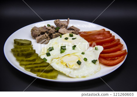 Delicious fresh tuna with eggs, tomatoes, cucmbers with green onion at the morning. Healthy and diet breakfast with tuna, eggs and vegetables on the white plate against dark background 121260603