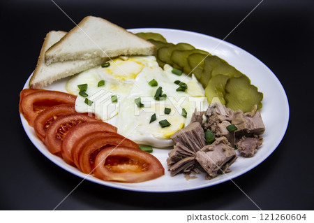 Delicious fresh tuna with eggs, bread, tomatoes, cucmbers with green onion at the morning. Healthy and diet breakfast with tuna, eggs and vegetables on the white plate against dark background Delicious fresh tuna with eggs, bread, tomatoes, cucmbers with green onion at the morning. Healthy and diet breakfast with tuna, eggs and vegetables on the white plate against dark background 121260604