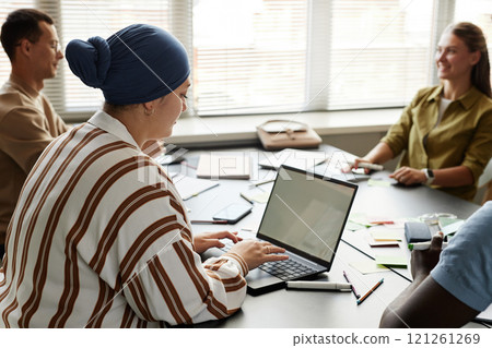 Side view of Muslim woman typing on laptop with blank mockup screen while studying sitting at desk in language course group, copy space 121261269