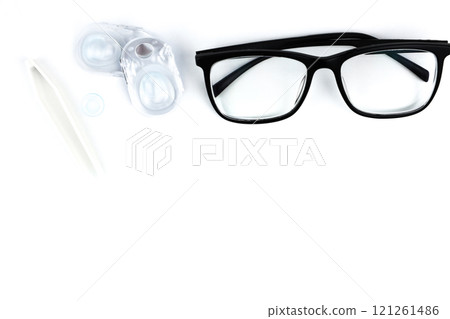 On top of the photo, there are close-up glasses in black frames, behind them disposable containers with contact lenses, a blue lens and beige tweezers in close-up on a white background with space for On top of the photo, there are close-up glasses in black frames, behind them disposable containers with contact lenses, a blue lens and beige tweezers in close-up on a white background with space for 121261486