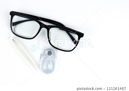 On the left of the photo, there are close-ups of black-framed glasses, behind them disposable containers with contact lenses, a blue lens and beige tweezers in close-up on a white background with 121261487