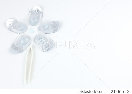Top and side view of a creative flower consisting of containers for daily contact lenses, in the center there is a soft bluish lens, down like the stem of a plant goes tweezers for taking lenses on a Top and side view of a creative flower consisting of containers for daily contact lenses, in the center there is a soft bluish lens, down like the stem of a plant goes tweezers for taking lenses on a 121261520