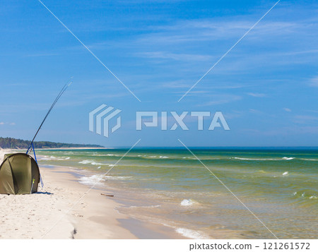 Fishing rod and tent on sea shore 121261572