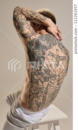 Back view of male athletic male body with tattoos, posing shirtless on chair against neutral studio background Back view of male athletic male body with tattoos, posing shirtless on chair against neutral studio background 121261957