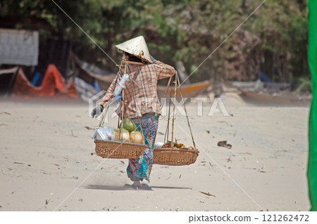 Vietnamese street vendor walking on sandy beach with traditional baskets and conical hat 121262472
