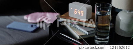 Website banner of nightstand with glass of water, books and alarm clock on top next to bed with sleep mask and smartphone Website banner of nightstand with glass of water, books and alarm clock on top next to bed with sleep mask and smartphone 121262612