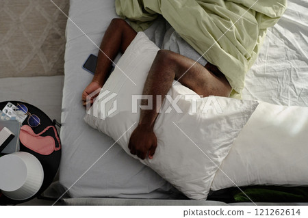 Top down shot of unrecognizable man hiding his head under soft white pillow while lying in bed Top down shot of unrecognizable man hiding his head under soft white pillow while lying in bed 121262614