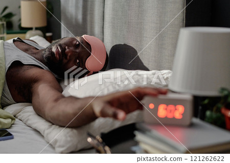 African American man with rose sleep mask on forehead stopping alarm in morning African American man with rose sleep mask on forehead stopping alarm in morning 121262622