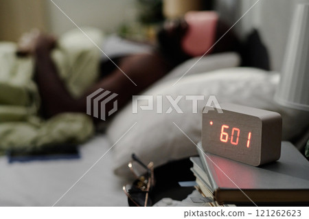 High angle shot of modern alarm clock on night stand next to bed with sleepy man 121262623