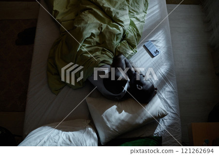 Top down shot of African American man sleeping tight in fetal position in bed Top down shot of African American man sleeping tight in fetal position in bed 121262694