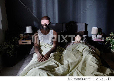 African American man with sleep mask getting up at night while his wife sleeping easy, he suffering from sleepwalking 121262717