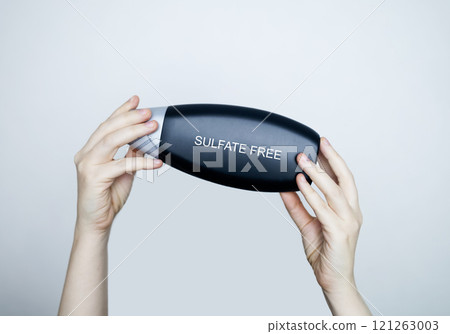 Female hands holding a can of shampoo, where it is written sulfate free, no sulfates. The concept of safe composition of shampoo without aggressive components Female hands holding a can of shampoo, where it is written sulfate free, no sulfates. The concept of safe composition of shampoo without aggressive components 121263003