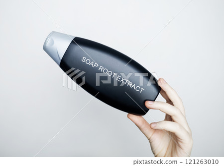 Female hands hold a bottle of shampoo, on which the ingredient is written - soap root extract. The concept of safe composition of organic shampoos 121263010