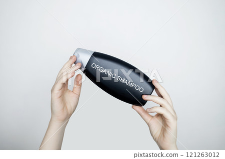 Female hands holding a bottle with the words - organic shampoo. Concept of safe composition and ingredients of environmentally friendly cosmetics and detergents 121263012