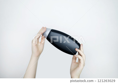 Female hands holding a can of shampoo with a blank label. White background, space for text. Composition of shampoo or conditioner 121263029