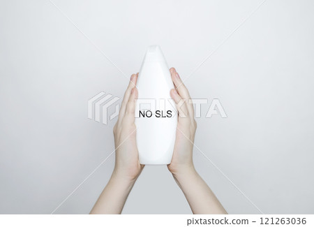 Female hands holding a can of shampoo, where it is written no sls, sls free. The concept of safe composition of shampoo without aggressive components 121263036