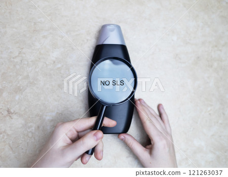 Female hands holding a can of shampoo, where it is written no sls, sls free. The concept of safe composition of shampoo without aggressive components 121263037