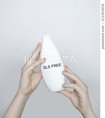 Female hands holding a can of shampoo, where it is written no sls, sls free. The concept of safe composition of shampoo without aggressive components 121263058