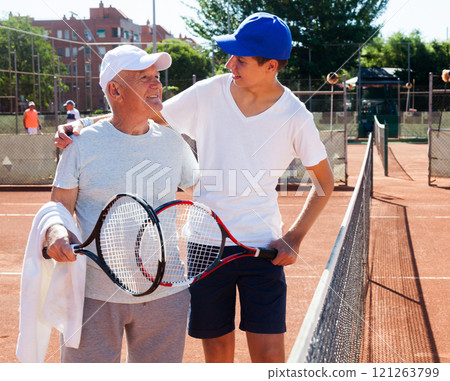 Grandfather and grandson talking on court playing tennis 121263799