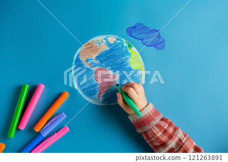Child's hand drawing a colorful globe with markers on a blue background 121263891